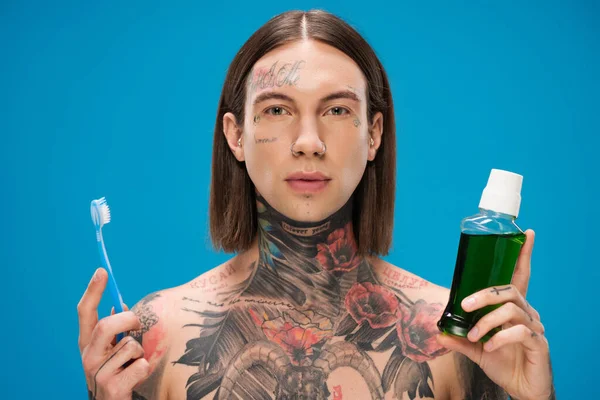 Молодой и татуированный мужчина с зубной щеткой и бутылкой с жидкостью для полоскания рта — стоковое фото