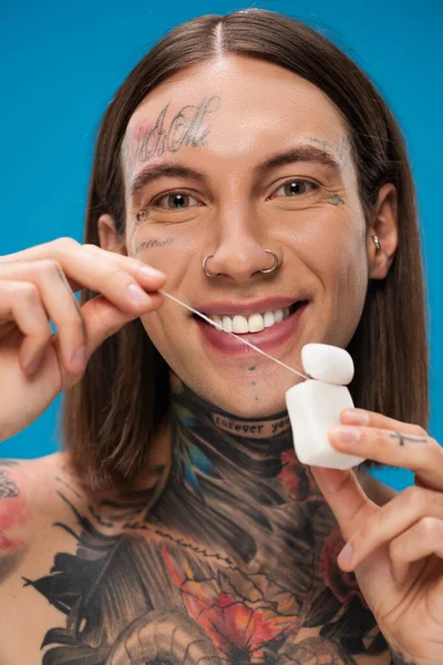 Cheerful and tattooed man holding dental floss isolated on blue — Stock Photo