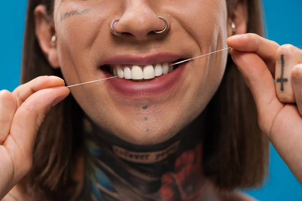 Vista recortada de alegre y tatuado hombre hilo dental dientes blancos aislados en azul - foto de stock