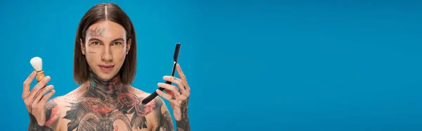 Молодой и татуированный мужчина с кисточкой для бритья и зеркалом, изолированные на голубом, баннер — стоковое фото