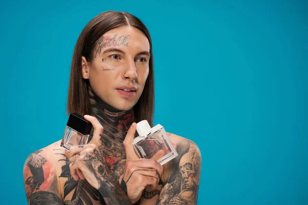 Shirtless and tattooed man holding bottles with perfume isolated on blue — Stock Photo