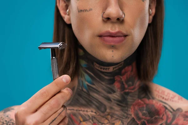 Cropped view of young man with tattoos holding safety razor isolated on blue — Stock Photo