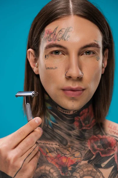 Young man with tattoos holding safety razor isolated on blue — Stock Photo