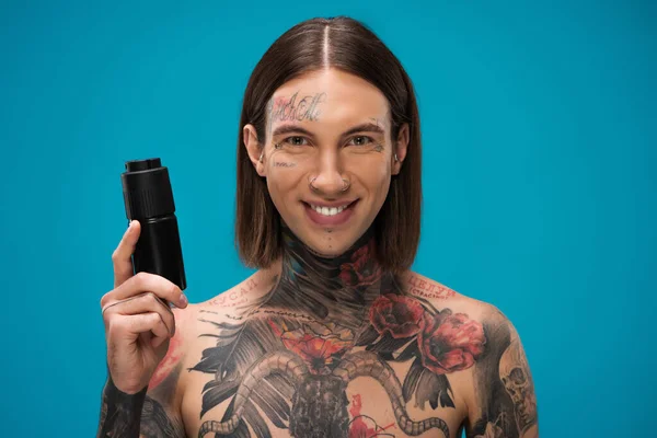 Happy and tattooed young man holding antiperspirant isolated on blue — Stock Photo