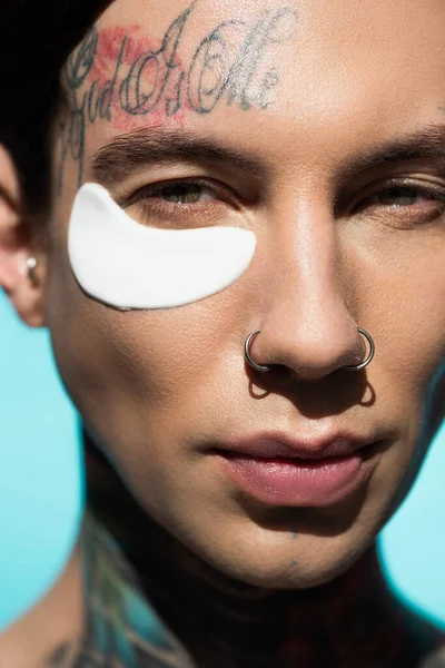 Close up of tattooed young man with eye patch looking at camera isolated on turquoise — Stock Photo