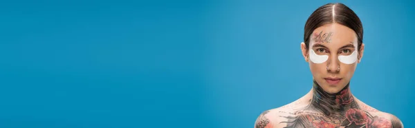 Shirtless and tattooed young man with eye patches looking at camera isolated on blue, banner — Stock Photo
