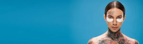 Jeune homme torse nu et tatoué avec des patchs pour les yeux regardant la caméra isolée sur bleu, bannière — Photo de stock