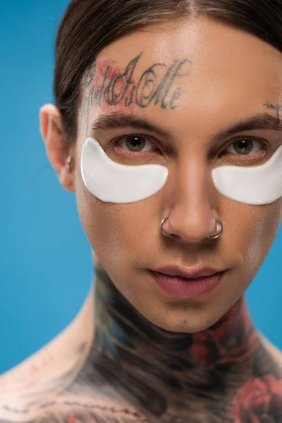 Close up of tattooed young man with eye patches looking at camera isolated on blue — Stock Photo