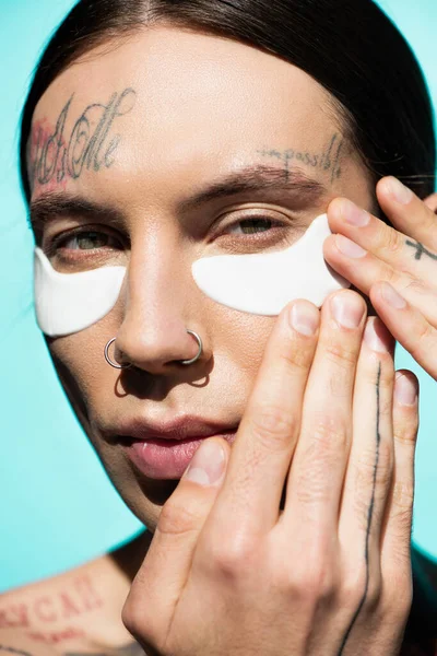 Close up de tatuado jovem aplicando manchas oculares isoladas em turquesa — Fotografia de Stock