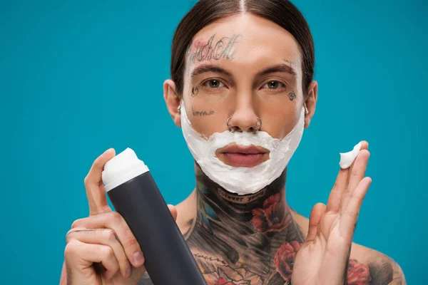 Jovem tatuado com espuma de barbear na cara segurando pode isolado em azul — Fotografia de Stock