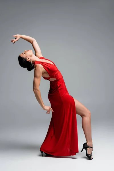 Vista lateral de bailarina de salón profesional en vestido rojo moviéndose sobre fondo gris - foto de stock