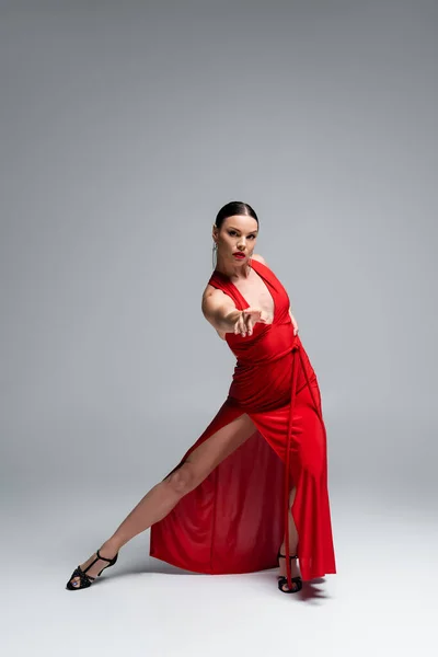 Повна довжина бального танцюриста в червоній сукні, дивлячись на камеру на сірому фоні — стокове фото