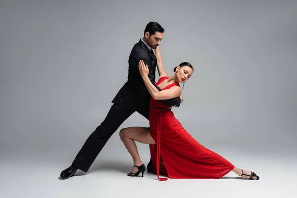 Bailarinas elegantes en traje y vestido realizando tango sobre fondo gris - foto de stock