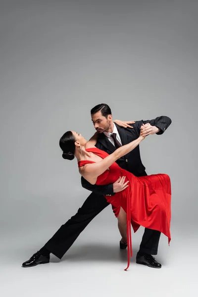 Elegante uomo in abito danza tango con partner su sfondo grigio — Foto stock