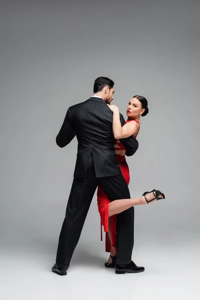 Full length of stylish dancer in heels performing tango with woman on grey background — Stock Photo