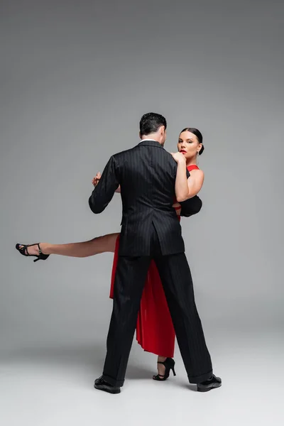 Elegant woman in heels looking at camera while dancing tango with partner on grey background — Stock Photo