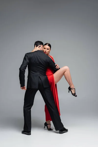 Elegant woman in red dress touching partner while dancing tango on grey background — Stock Photo