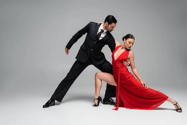 Hombre de traje abrazando a su pareja mientras baila tango sobre fondo gris - foto de stock