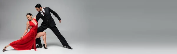 Elegante hombre de traje realizando tango con mujer sobre fondo gris, estandarte - foto de stock