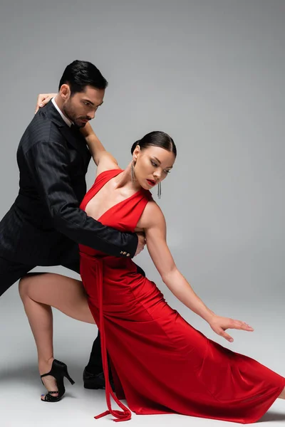 Mann im eleganten Anzug tanzt Tango mit Partnerin im Kleid auf grauem Hintergrund — Stockfoto