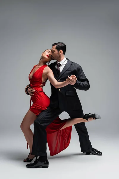 Full length of professional ballroom dancers performing tango on grey background — Stock Photo