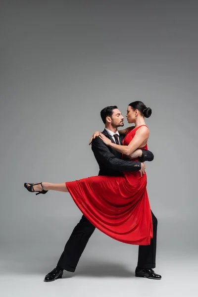 Vue latérale du danseur tenant partenaire en robe rouge sur fond gris — Photo de stock
