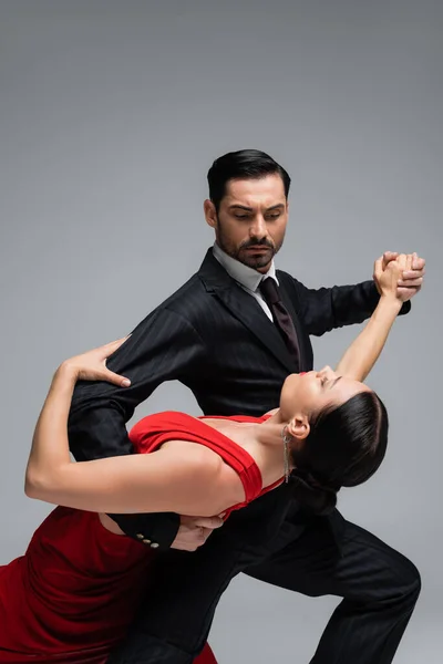 Hombre de traje bailando tango con pareja morena aislada sobre gris - foto de stock