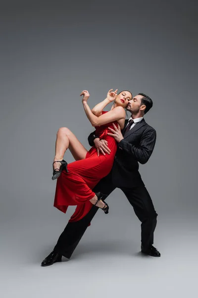 Full length of stylish couple performing tango on grey background — Stock Photo
