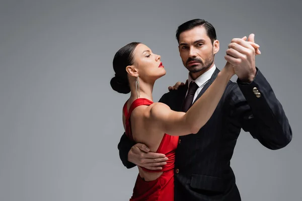 Hombre de traje mirando a cámara mientras baila tango con pareja aislada en gris - foto de stock