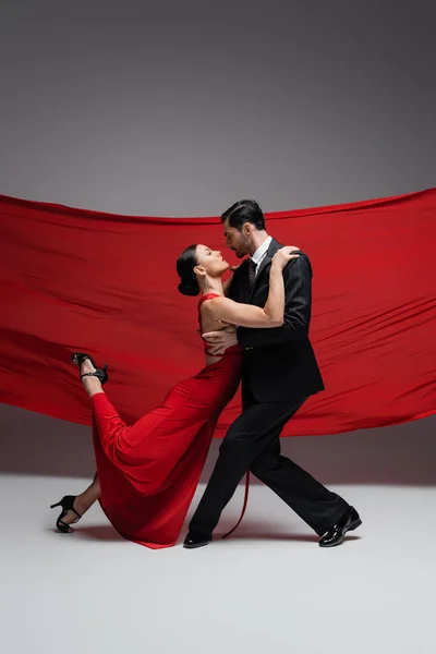 Vista lateral de bailarines de salón realizando tango sobre fondo gris con tela roja - foto de stock