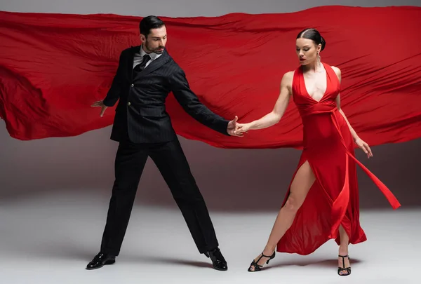 Professional ballroom dancers holding hands on grey background with red fabric — Stock Photo