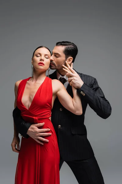 Passionate man in suit dancing tango with elegant partner isolated on grey — Stock Photo