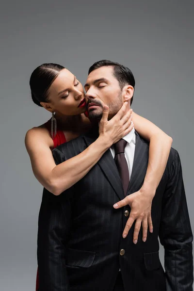 Brunette femme aux lèvres rouges touchant homme élégant isolé sur gris — Photo de stock