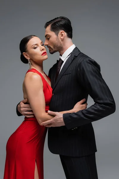 Hombre de traje abrazando elegante novia con labios rojos aislados en gris - foto de stock