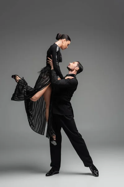 Side view of professional ballroom dancer lifting partner on grey background — Stock Photo