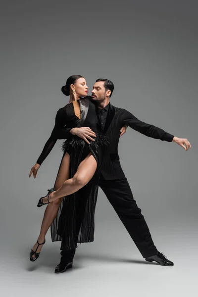 Bailarines de salón profesionales en trajes negros realizando tango sobre fondo gris - foto de stock