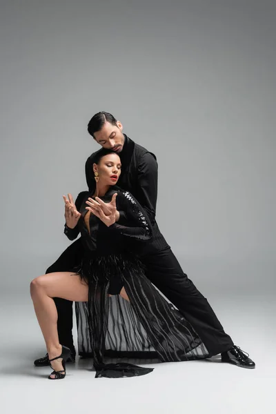 Elegant dancer performing tango with partner in black dress on grey background — Stock Photo