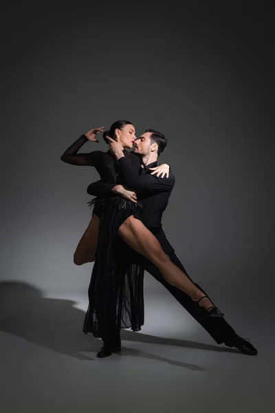 Seitenansicht professioneller Tänzer, die Tango auf grauem Hintergrund mit Beleuchtung aufführen — Stockfoto