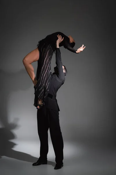 Dancer lifting partner in black dress on grey background with shadow — Stock Photo