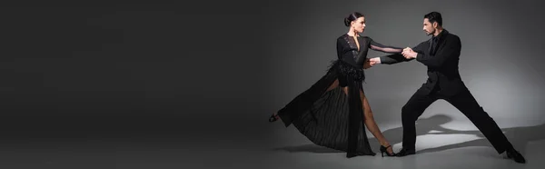 Side view of ballroom dancers holding hands while dancing on grey background with shadow, banner — Stock Photo