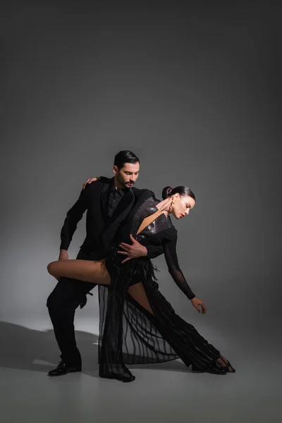 Elegante Tänzerin umarmt brünetten Partner in schwarzem Kleid auf grauem Hintergrund mit Beleuchtung — Stockfoto