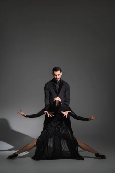 Dançarina de terno realizando tango com mulher de vestido preto em fundo cinza com sombra — Fotografia de Stock