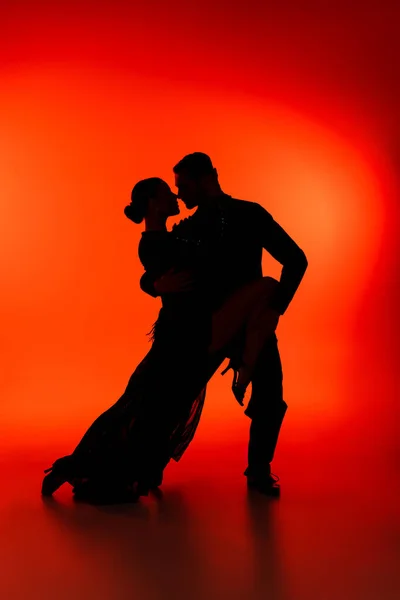 Vista lateral de silueta de pareja bailando tango sobre fondo rojo - foto de stock