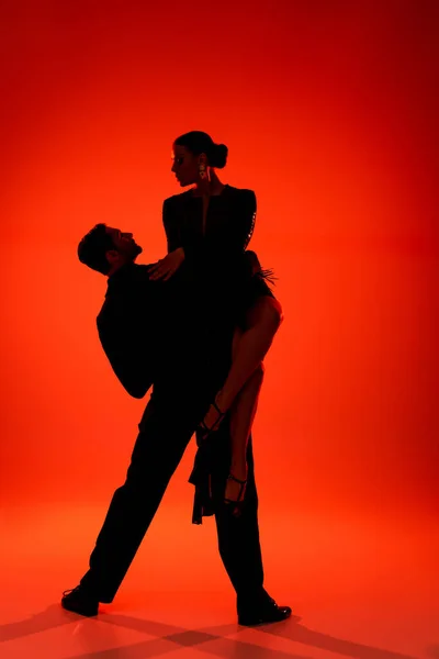 Silhouette of professional couple of dancers performing tango on red background — Stock Photo