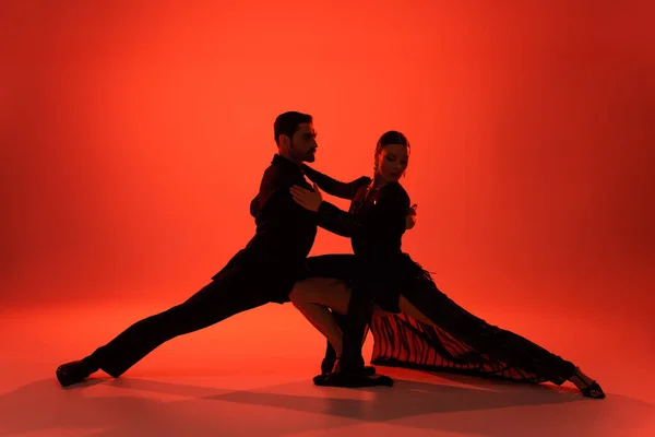 Silhouette of elegant couple dancing tango on red background — Stock Photo