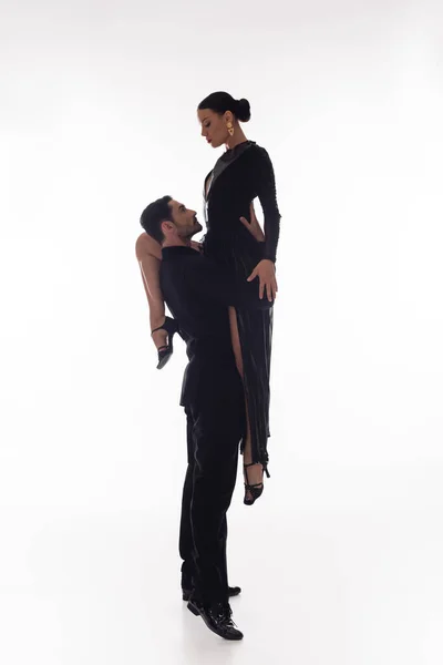 Side view of man in suit lifting partner in dress on white background — Stock Photo