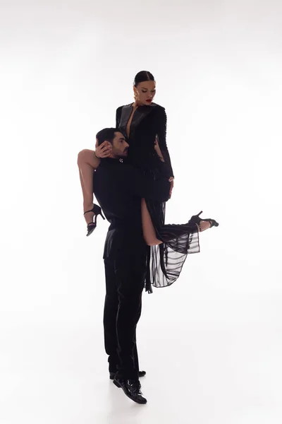 Brünette Tänzerin hebt Partner in schwarzem Kleid auf weißem Hintergrund — Stockfoto