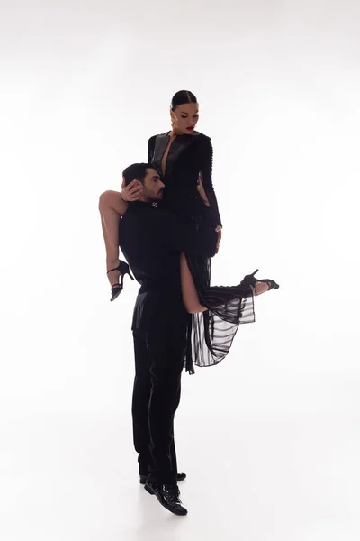Brunette dancer lifting partner in black dress on white background — Stock Photo