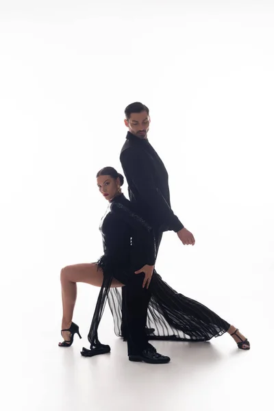 Mulher elegante em vestido preto realizando tango com parceiro no fundo branco — Fotografia de Stock