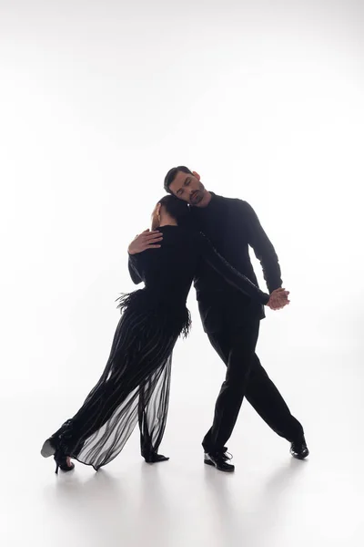 Bailarina de salão abraçando parceiro no vestido enquanto dança tango no fundo branco — Fotografia de Stock
